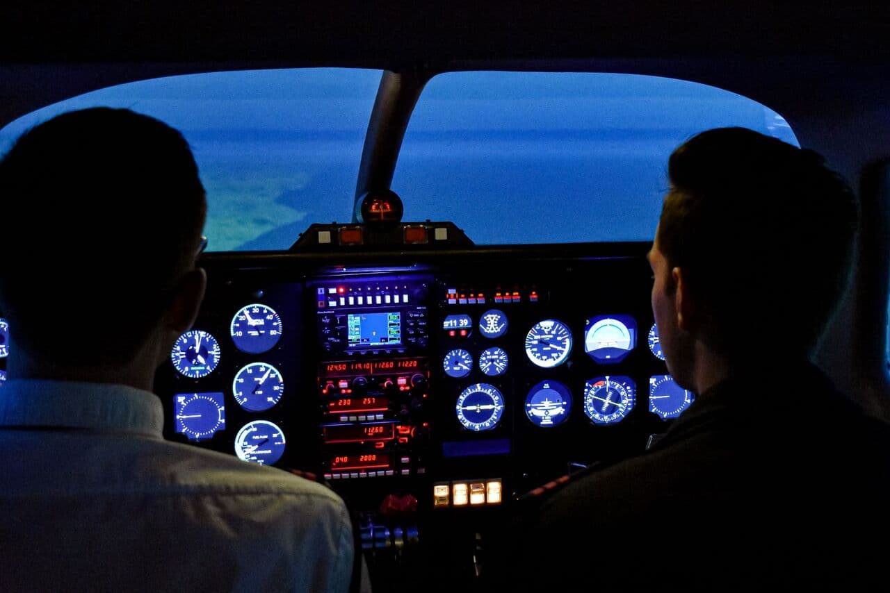 Two pilots in a softly lit cockpit before dawn, the instruments glowing
