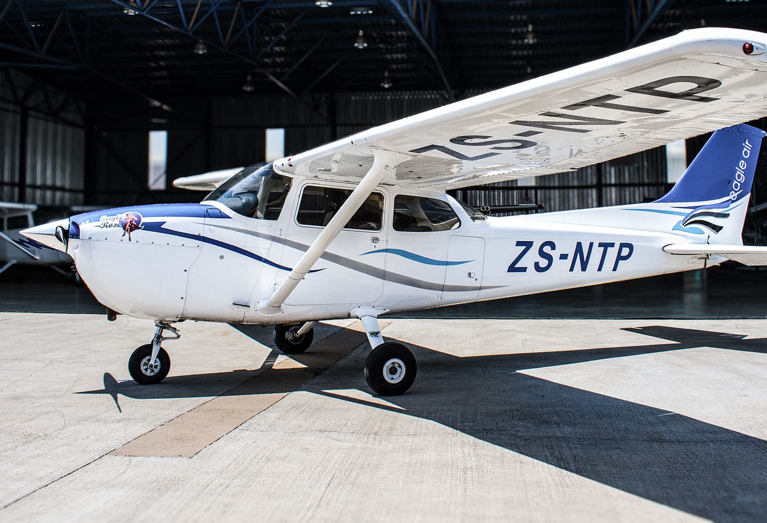 A Cessna 172 on the sunlit apron outside the Eagle Air hangar