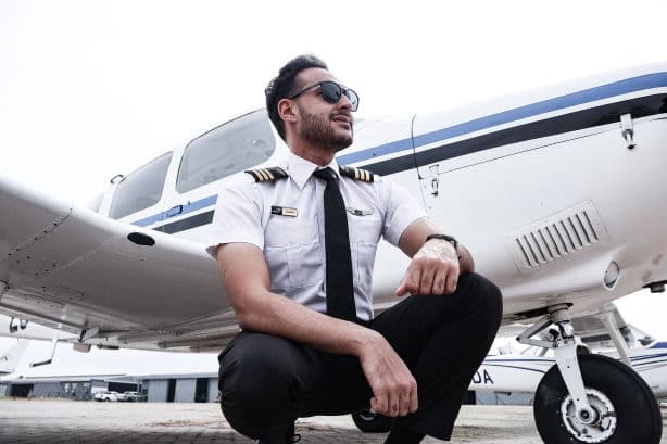 A young pilot crouched beside an aircraft on the apron, looking across the airfield